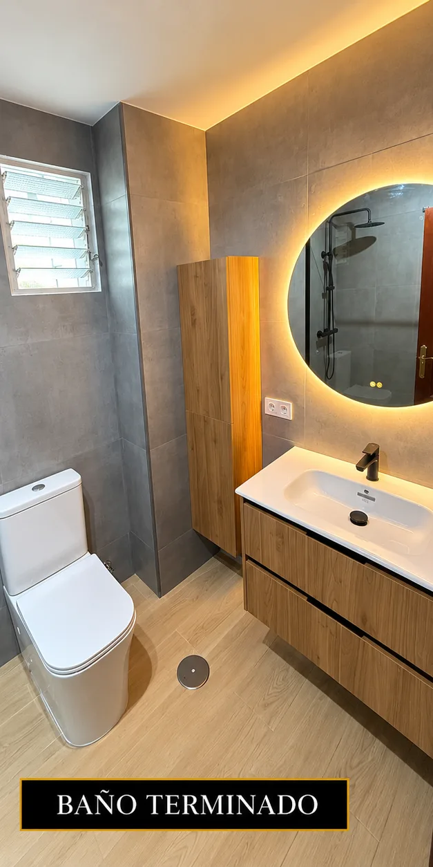 Baño de diseño con espejo redondo retroiluminado y mueble de madera, obra de Elixir Construcción en Sevilla